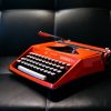 A bright red typewriter on a leather sofa.