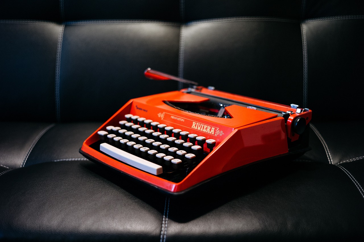 A bright red typewriter on a leather sofa.